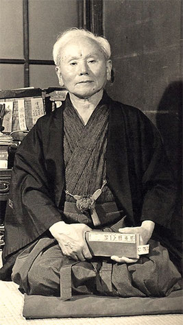Historisches Porträt von Gichin Funakoshi, Begründer des Shotokan-Karate, in traditioneller Kleidung im Seiza auf Tatami.